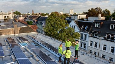 4 Personen in Jacken sprechen miteinander an der Decke eines Gebäudes mit Fotovoltaikanlagen.