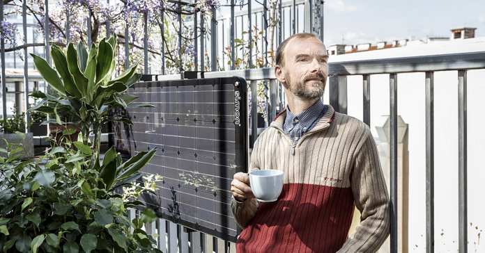 Mann lehnt mit einer Tasse in der Hand an einem Balkongeländer, das mit der Balkon-PV-Anlage Simon ausgestattet ist.