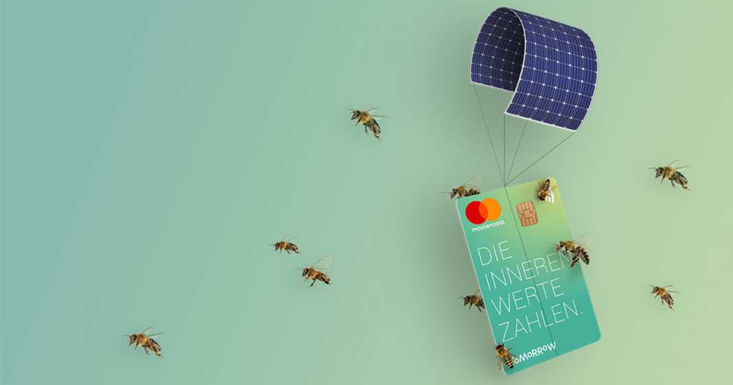 Eine Kreditkarte vor grünem Hintergrund die getragen wird durch ein Solarpanel als Fallschirm und dabei von einem Schwarm Bienen begleitet wird.
