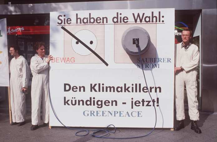 zwei Frauen und ein Mann stehen neben einem Menschengroßen Plakat, auf dem steht: 