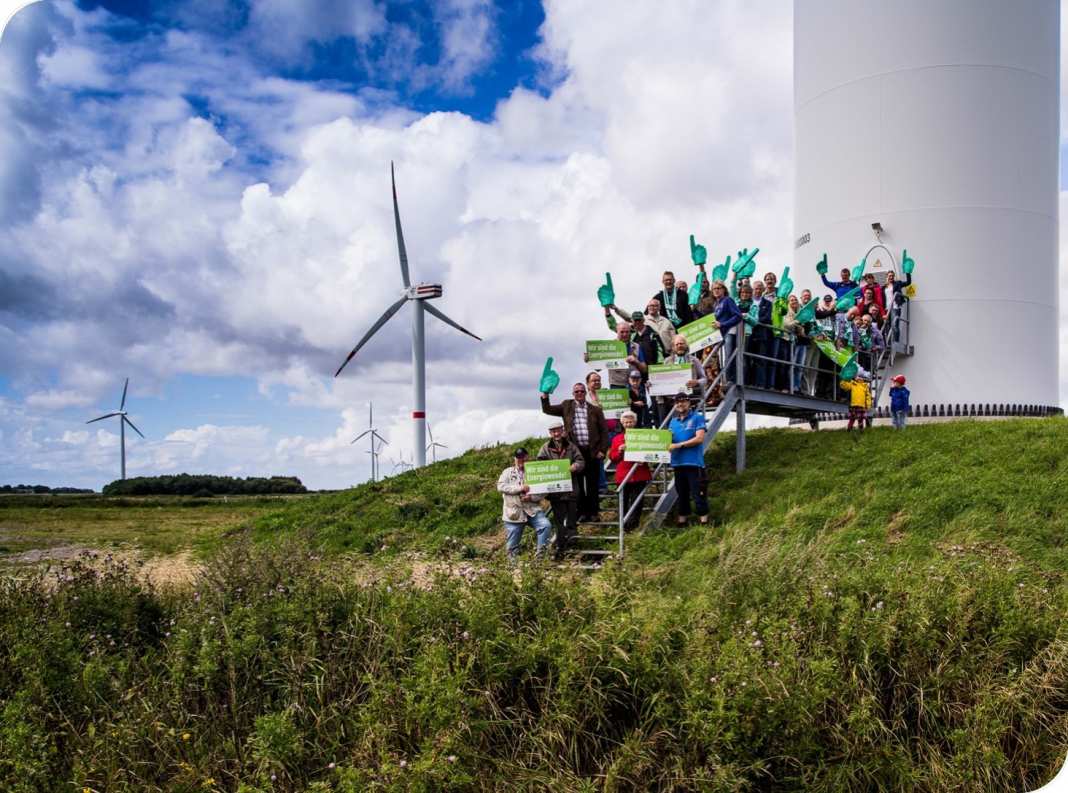 Eine Gruppe Bürger:innen auf einem Hügel vor einem Windrad.