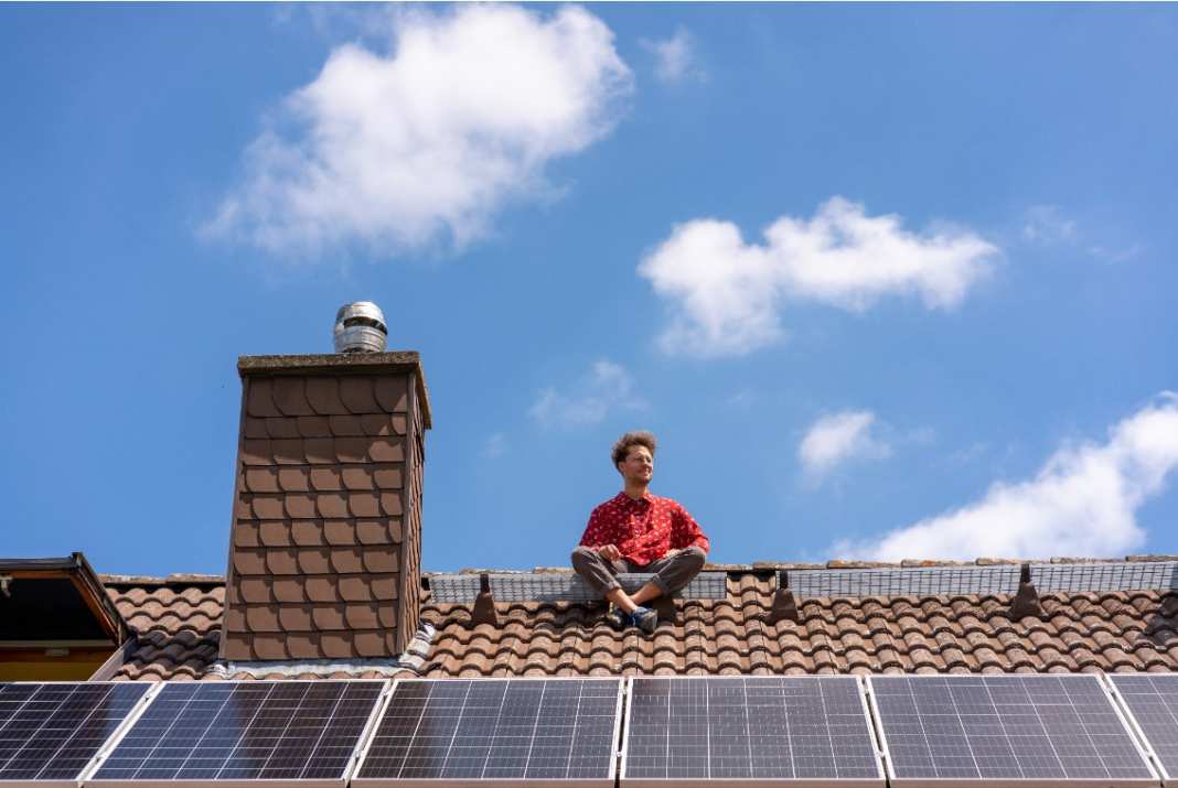 Ein Mann sitzt auf einem Dach mit Solarpanelen.