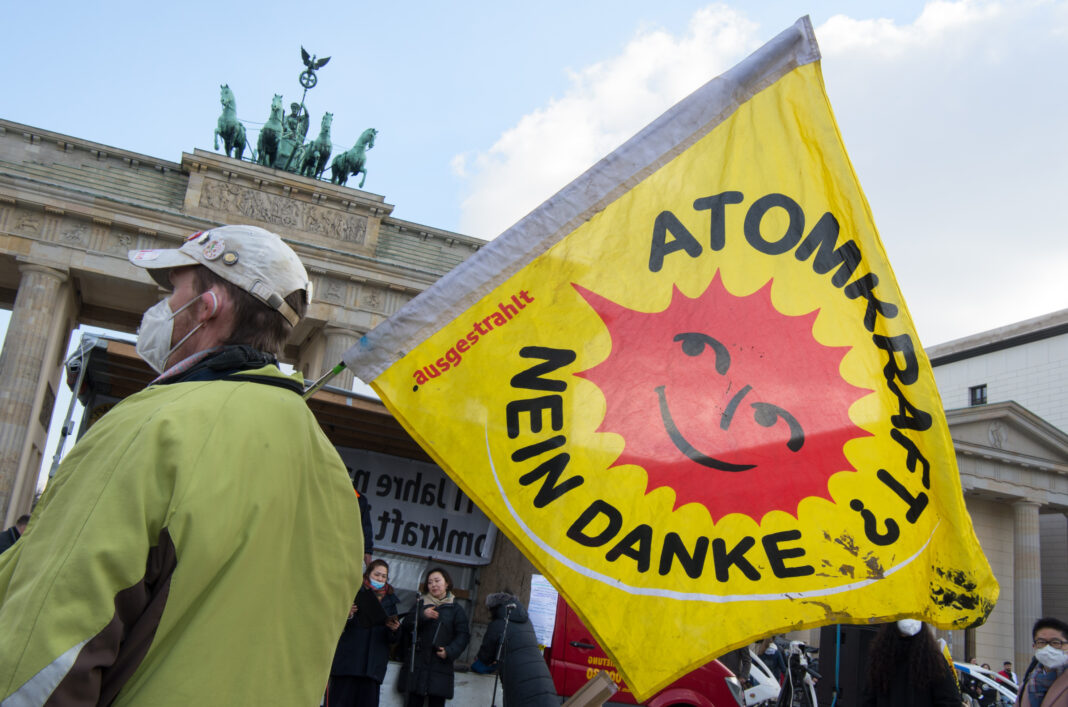 Person mit FFP2-Maske und Atomkraft? Nein Danke Fahne vor dem Brandenburger Tor in Berlin