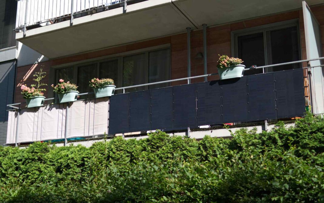 Ein Balkon mit blumig bepflanzten Pflanzkübeln und Balkonkraftwerk am Geländer. Die Sonne scheint.