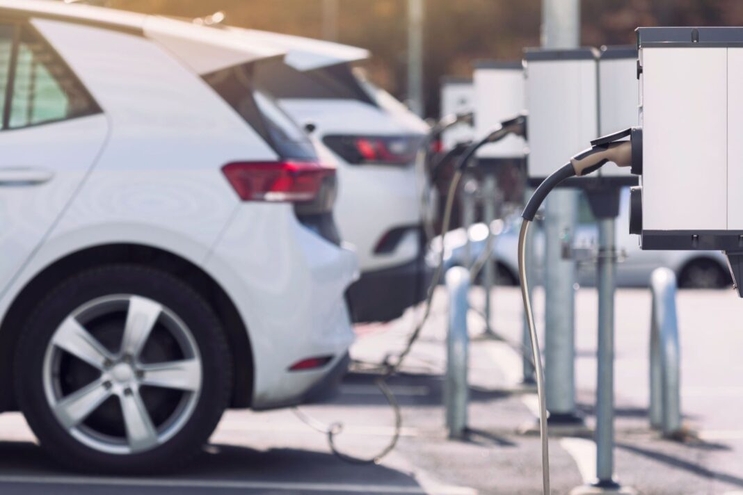 Weiße Elektroautos stehen auf einem Parkplatz und sind an weiße moderne Ladesäulen angeschlossen.