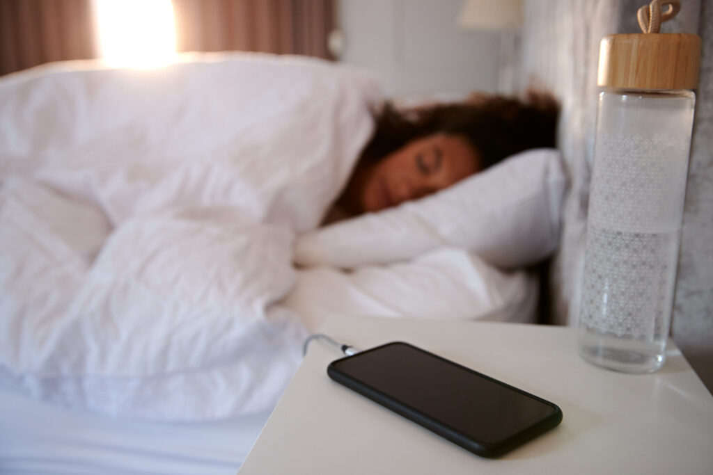 Frau schläft im Bett mit Mobiltelefon auf dem Nachttisch.