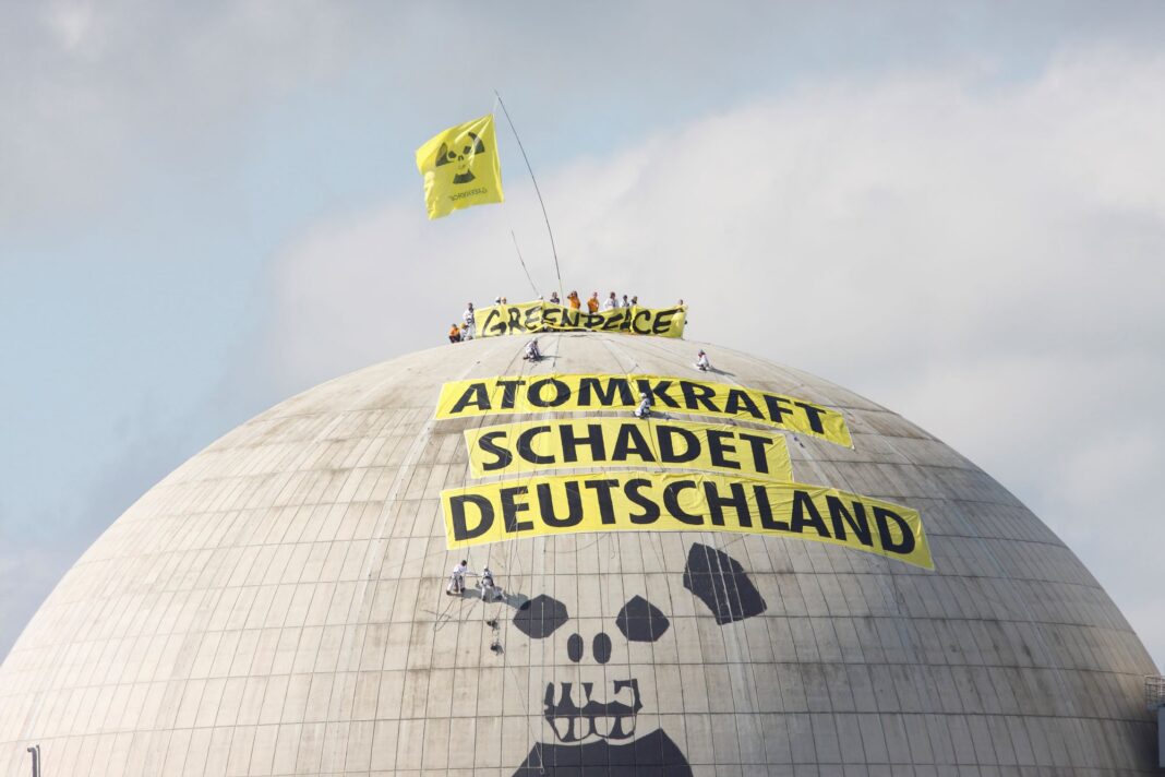 Eine Gruppe von Menschen hat ein riesiges gelbes Banner mit der Aufschrift „Atomkraft schadet Deutschland“ auf einem Kuppelgebäude angebracht. Oben steht „Greenpeace“, eine Flagge weht.