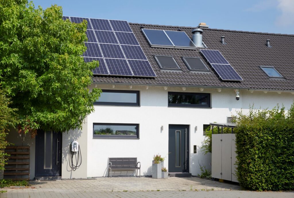 Modernes Einfamilienhaus mit PV-Anlage auf dem Dach und Wallbox vor der Tür.