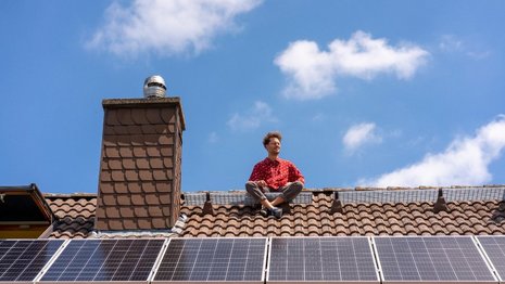 Ein Mann sitzt auf einem Dach mit Solarpanelen.
