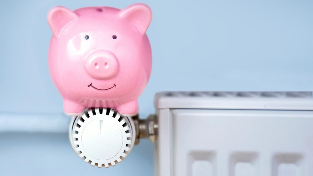Rosa Sparschwein sitzt auf Heizungsthermostat.