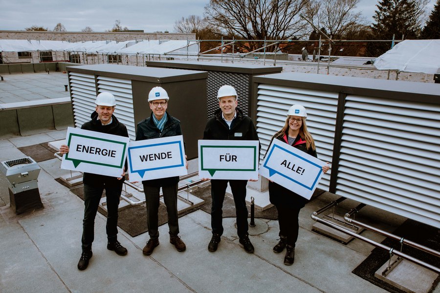 Vertreter:innen von Green Planet Energy und Fördern & Wohnen stehen auf dem Dach eines Hauses in der Wichmannstraße. Sie halten Plakate mit dem Text "ENERGIEWENDE FÜR ALLE!"