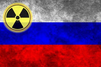 Bildfüllend die russische Flagge mit einem gelb-schwarzen Zeichen für Atom in der linken oberen Ecke