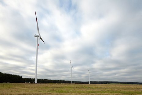 Drei Windkraftanlagen auf einer Ebene vor einem bewaldeten Gebiet