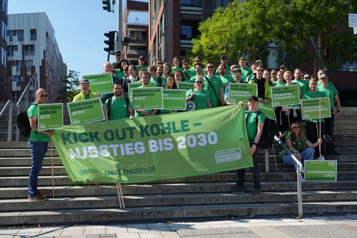 Ein Gruppenfoto von Personen in grünen T-Shirts und Bannern auf einer Treppe. Auf den Bannern ist das Logo von Green Planet Energy zu sehen.