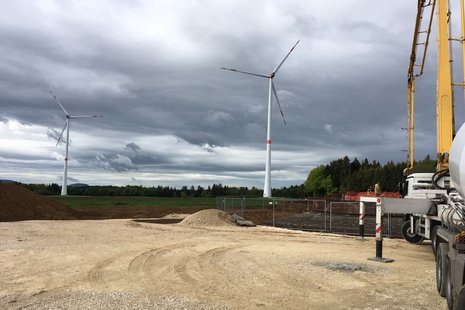 Baustelle mit zwei Windkraftanlagen im Hintergrund. Rechts ein Baufahrzeug.