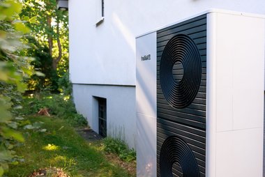 Wärmepumpe steht direkt an einem Bestands-Gebäude im Garten.
