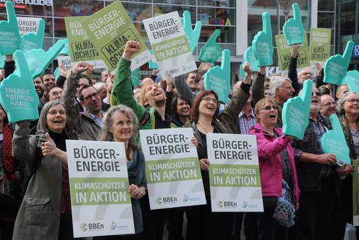 Eine Menschenmenge hält Plakate mit der Aufschrift „Bürger-Energie, Klimaschützer in Aktion“ hoch.