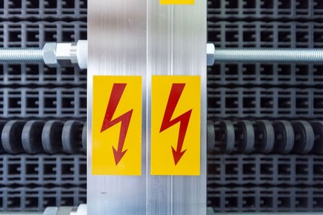 Elektrolyseur in der Nahansicht mit zwei Blitz-Symbolen als Zeichen für Hochspannung