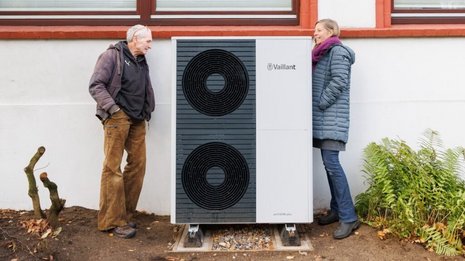 Ein Mann und eine Fraue stehen links und recht neben einer großen Wärmepumpe mit zwei Ventilatoren