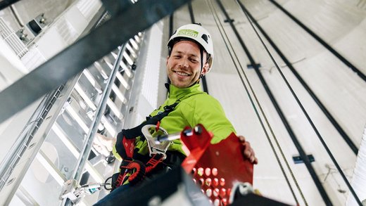 Eine Person mit Green Planet Energy Jacke klettert eine Leiter in einer Art vertikaler Röhre hoch.