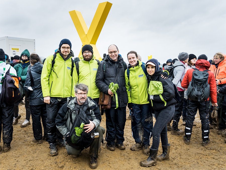 6 Personen in wasserdichten Stiefeln auf einem schlammigen Feld schauen in die Kamera.