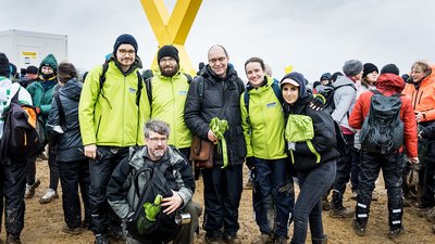 6 Personen in wasserdichten Stiefeln auf einem schlammigen Feld schauen in die Kamera.
