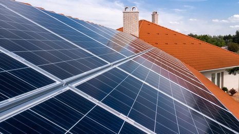 PV-Anlage auf einem Dach mit tonfarbenen Ziegeln. Im Hintergrund sind weitere Häuser mit der gleichen Dachfarbe zu sehen.