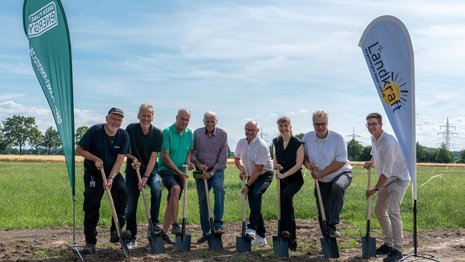 Mehrere Personen beim symbolischen Spatenstich für den Solarpark Dedendorf auf einer Freifläche.