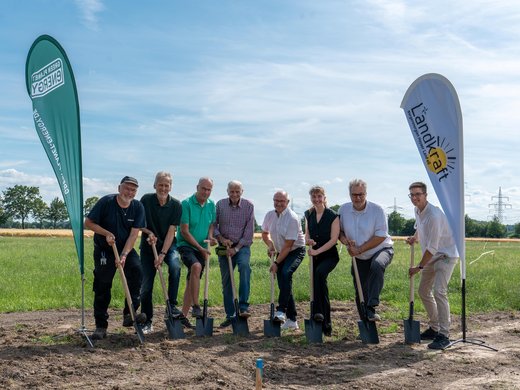 Mehrere Personen beim symbolischen Spatenstich für den Solarpark Dedendorf auf einer Freifläche.