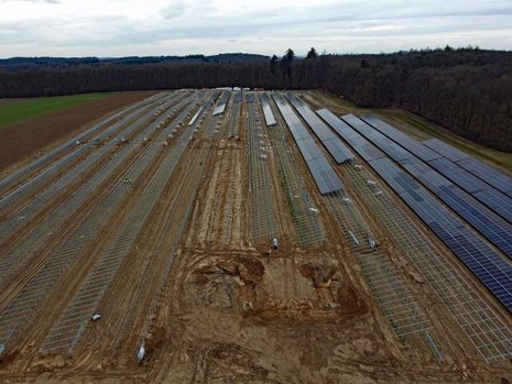Braunes Feld mit Solaranlagen im Bau. Die Hälfte der Halterungen sind mit Solarpaneelen bestückt.