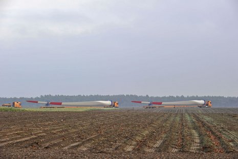 2 Lastwagen transportieren 2 Windradflügel durch ein Feld.