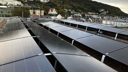 Nahaufnahme von Photovoltaikmodulen auf einem Flachdach, mit einer hügeligen Wohngegend im Hintergrund.