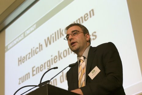 Mann spricht an Rednerpult in ein Mikro. Im Hintergrund ist eine Power Point Präsentation mit dem Titel "Herzlich Willkommen zum Energiekongress"