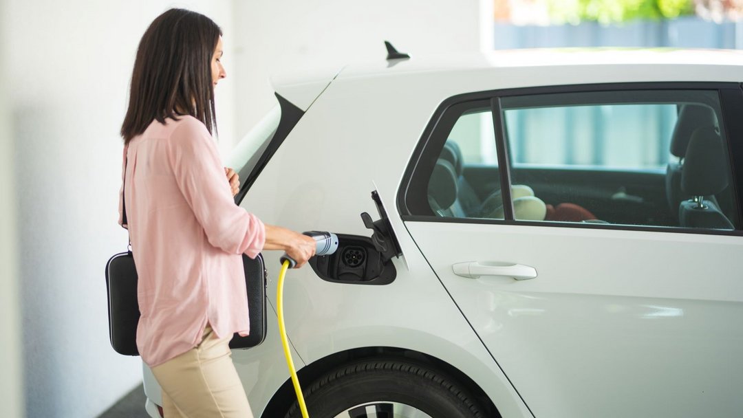 Frau lädt ein weißes Elektroauto mit einem gelben Kabel in einer hellen Garage auf.
