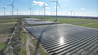 Solarpark mit Windrädern in weiter Landschaft bei klarem Himmel.