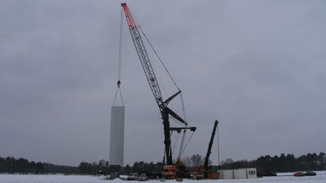 Ein Kran hebt den Mast einer Windkraftanlage in die Höhe.