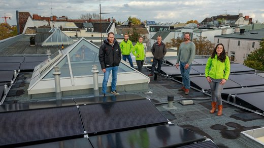 Mehrere Personen stehen inmitten einer Solaranlage auf einem Flachdach und lächeln in die Kamera.