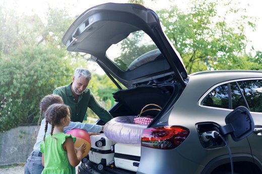 Vater mit zwei Töchtern laden Gepäck in den Kofferraum eines Autos.