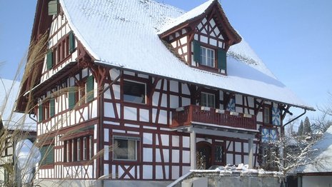 Fachwerkhaus mit rötlichem Holz und grünen Fensterläden im Schnee.