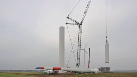 Ein Kran hebt einen Teil des Mastes der Windkraftanlage an, während ein Flügel im Vordergrund liegt.