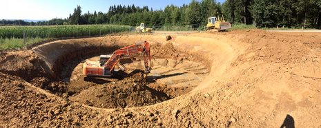 Rundliche Erdgrube, in der ein Bagger Erde aushebt