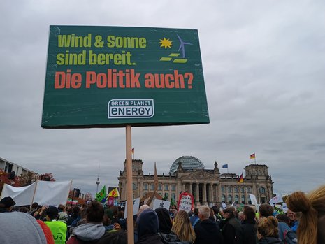 Zahlreiche Demonstrierende mit Schildern aus den Erneuerbaren Energien, zentral im Hintergrund der Reichstag. Davor das Demo-Schild mit der Aufschrift "Wind & Sonne sind bereit. Die Politik auch?" von Green Planet Energy.