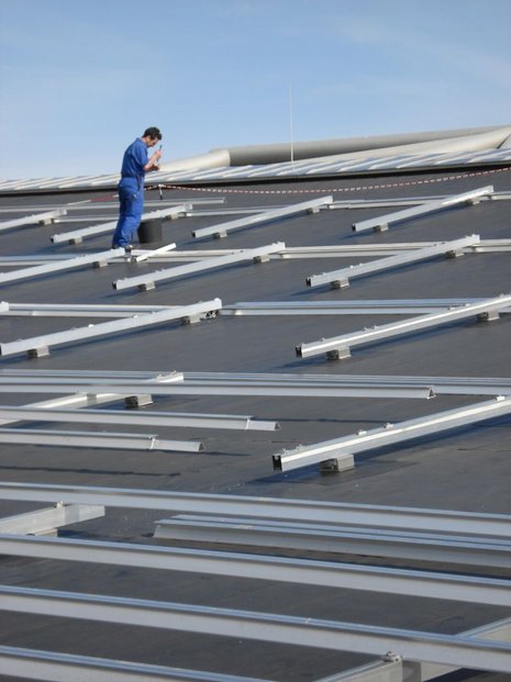 Ein Mann steht auf einem Dach zwischen Metallhalterungen für Photovoltaikmodule