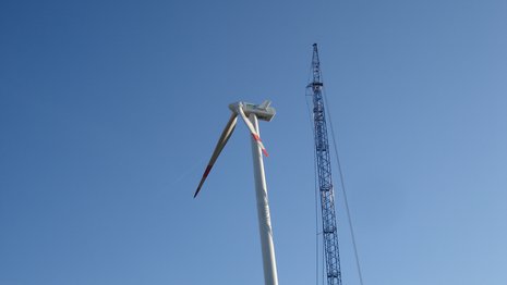 Windkraftanlage mit zwei Rotorblättern neben einem Kran