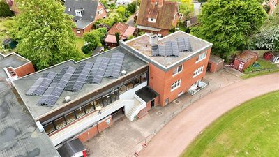 Gebäudekomplex mit mehreren Solaranlagen auf den Dächern, umgeben von Wohnhäusern und Grünflächen.