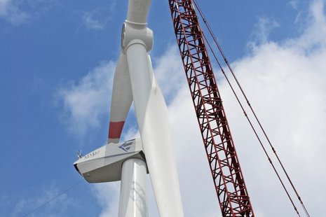 Foto von unten von der Montage der Windturbinenflügel mithilfe eines roten Krans.