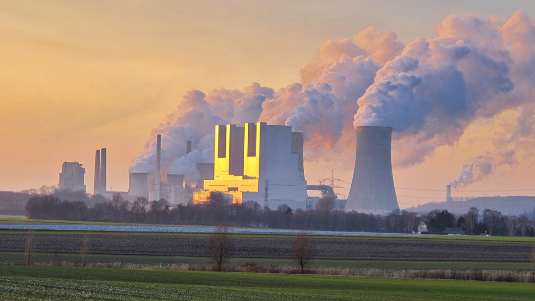 Mehrere Kühltürme eines Kohlekraftwerks mit Dampfwolken werden von der Sonne in der Dämmerung angestrahlt 