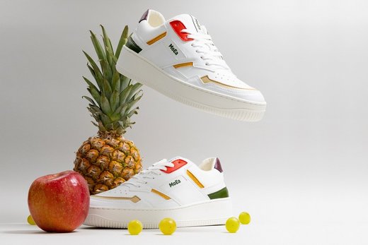 Weiße Sneaker umgeben von einer Ananas, einem Apfel und fünf einzelnen Weintrauben. Ein Sneaker schwebt über dem Ganzen.