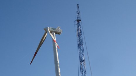 Windkraftanlage mit zwei Rotorblättern neben einem Kran