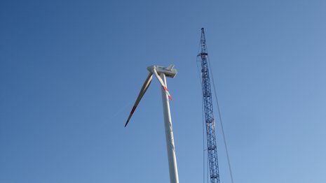 Windkraftanlage mit zwei Rotorblättern neben einem Kran